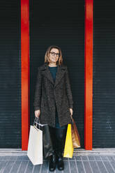 Frau mit Einkaufstüten vor einer Wand stehend - MRRF01827