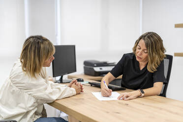 Doctor writing on paper while talking to patient in clinic - DLTSF02520