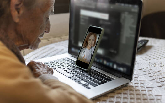 Ältere Frau konsultiert Arzt per Videoanruf über Smartphone zu Hause - JCCMF04932