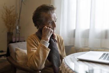 Nachdenkliche ältere Frau sitzt zu Hause vor ihrem Laptop - JCCMF04933