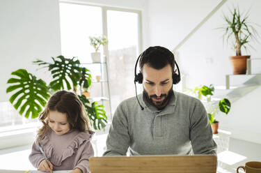 Mann mit Headset benutzt Laptop bei seiner Tochter zu Hause - JCCMF04945