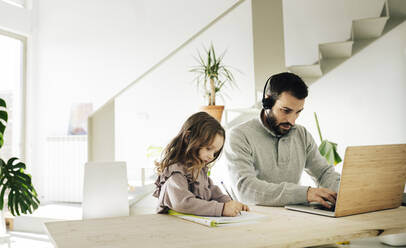 Father working by daughter drawing on book at home - JCCMF04947