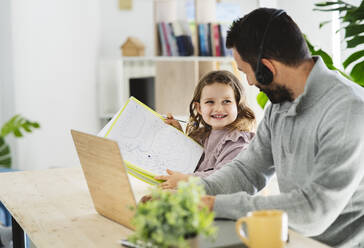 Lächelndes Mädchen zeigt dem Vater, der zu Hause arbeitet, eine Zeichnung - JCCMF04948