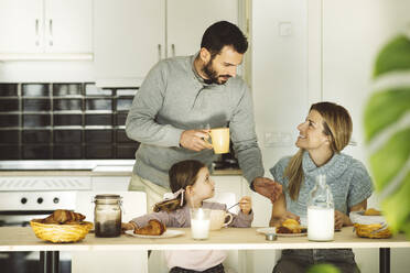 Man talking to woman sitting by daughter at breakfast table - JCCMF04966