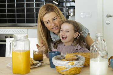 Mother pointing at juice talking to happy daughter - JCCMF04967