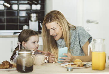 Mother with mobile phone talking to daughter at home - JCCMF04970