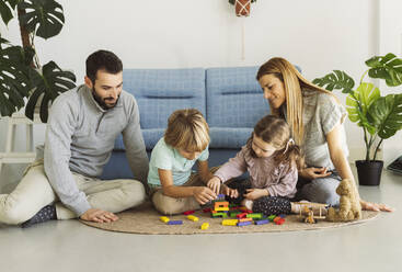 Brother and sister playing toy blocks with parents in living room - JCCMF04976