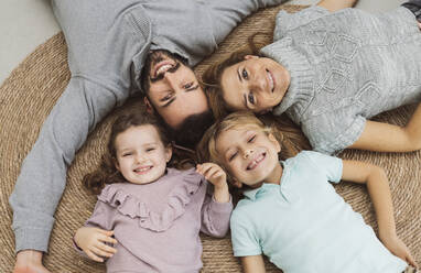 Happy family lying together on rug at home - JCCMF04978