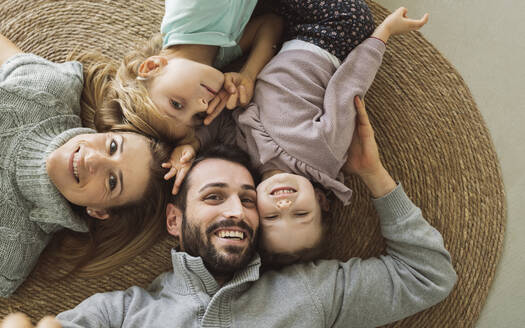 Glückliche Eltern mit Kindern, die zu Hause auf dem Teppich liegen - JCCMF04979