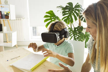 Junge trägt VR-Headset und gestikuliert bei seiner Mutter zu Hause - JCCMF04983