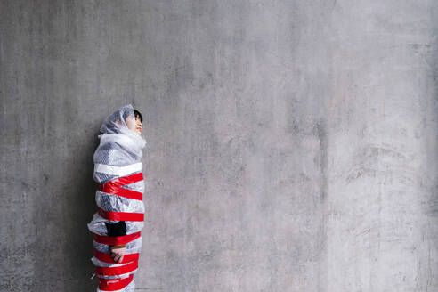 Frau in Luftpolsterfolie lehnt an grauer Wand - ASGF02037