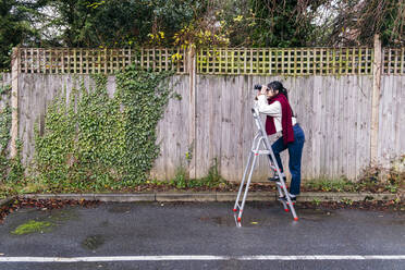 Woman standing on ladder looking through binoculars - ASGF02065