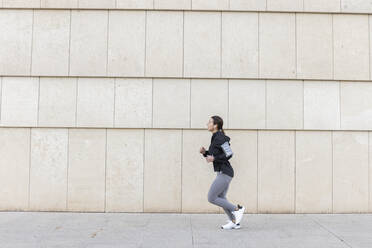 Active woman jogging on footpath by wall - JPTF01001