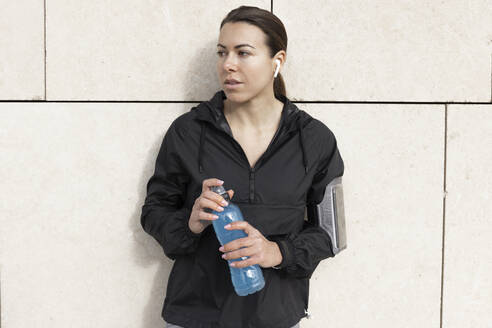 Frau mit Wasserflasche vor einer Wand stehend - JPTF01004