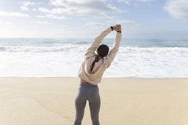 Sportswoman stretching arms at beach on sunny day - JPTF01006