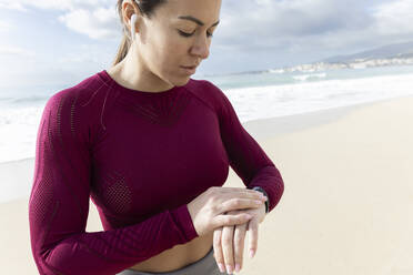 Sportlerin prüft am Strand den Puls auf ihrer Smartwatch - JPTF01007
