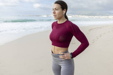 Fit woman standing with hands on hips at beach - JPTF01009