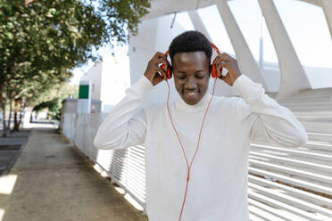 Smiling man wearing headphones on footpath - TCEF02154