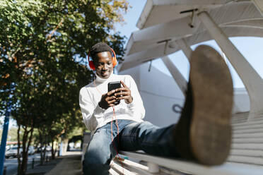 Smiling man wearing headphones using smart phone on railing - TCEF02162