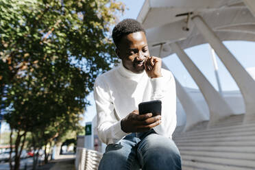 Smiling young man using mobile phone on railing - TCEF02164