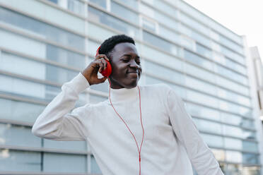 Smiling young man listening music through orange headphones - TCEF02165