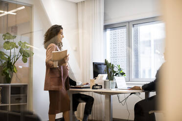 Schwangere Chefin mit Notizblock, die mit Kollegen im Büro diskutiert - MASF27984