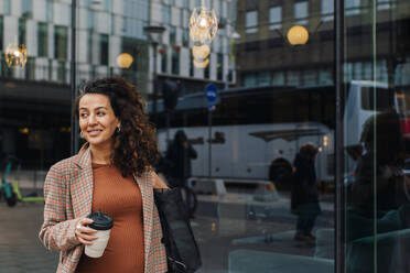 Smiling pregnant businesswoman with disposable coffee cup in city - MASF28016