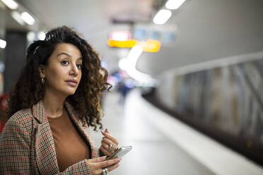 Female entrepreneur with smart phone waiting for train at station - MASF28017