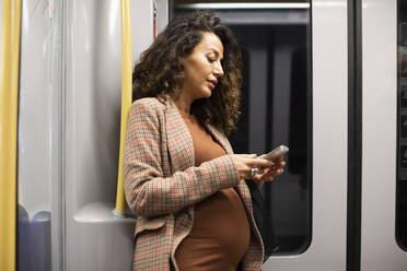 Pregnant female entrepreneur using smart phone while traveling by train - MASF28019