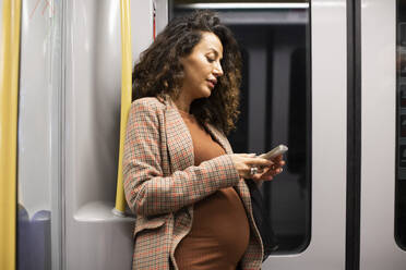 Schwangere Unternehmerin bei der Nutzung eines Smartphones während einer Zugfahrt - MASF28019