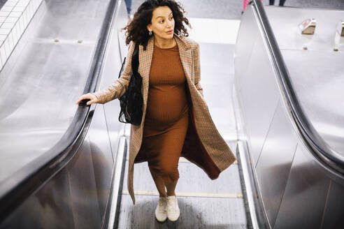 Schwangere Geschäftsfrau schaut weg, während sie auf der Rolltreppe im Bahnhof fährt - MASF28028