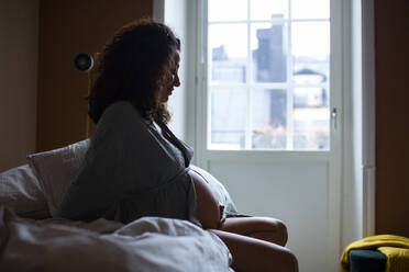 Pregnant woman sitting on bed in bedroom - MASF28031