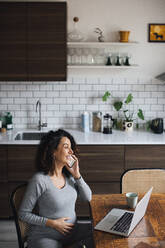 Smiling businesswoman talking on smart phone while working at home - MASF28044