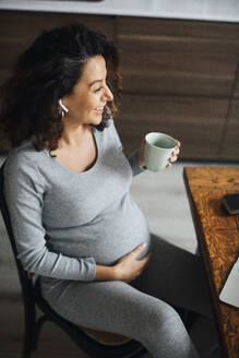 Schwangere Freiberuflerin im Gespräch über Bluetooth bei einem Kaffee zu Hause - MASF28045