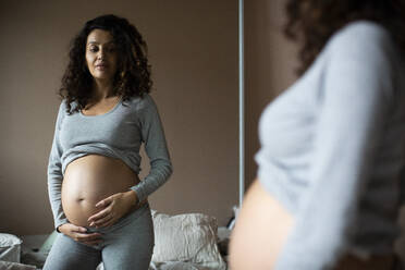 Pregnant woman looking in mirror at home - MASF28051