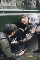 Vater wechselt Reifen, während er mit seinem Sohn in der Einfahrt spricht - MASF28081