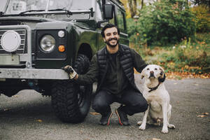 Porträt eines lächelnden Mannes mit Hund an einem Geländewagen - MASF28108