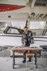 Portrait of mature man using smart phone at table in garage - MASF28122