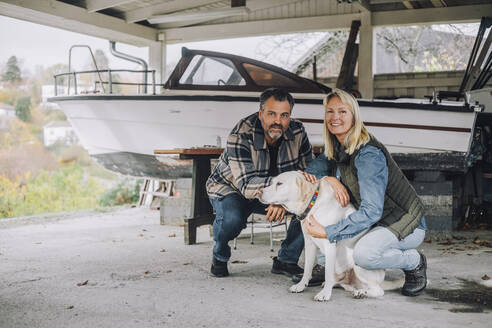 Portrait of smiling male and female friends with dog in garage - MASF28131