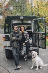 Portrait of smiling heterosexual couple with dog against sports utility vehicle - MASF28139