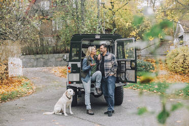 Mature male and female friends looking at each other by sports utility vehicle - MASF28140