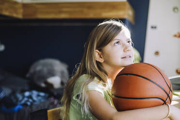 Girl looking up while sitting with basketball at home - MASF28160