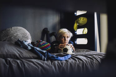 Contemplative boy with soccer ball lying on bed at home - MASF28164