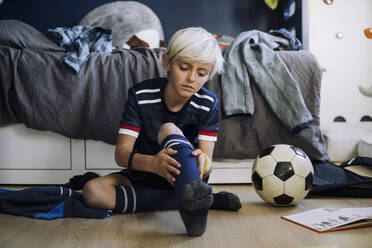 Blonder Junge trägt Socken, während er im Schlafzimmer zu Hause sitzt - MASF28171