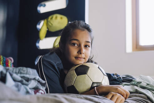 Porträt eines Mädchens mit Fußball, das zu Hause auf dem Bett liegt - MASF28177