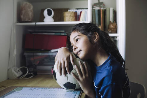 Contemplative girl looking away with soccer ball at table - MASF28178