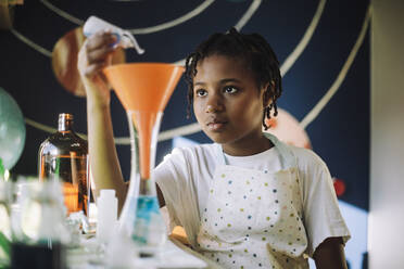 Fokussierte Schülerin, die eine Chemikalie durch einen Trichter gießt, während sie ein wissenschaftliches Projekt zu Hause durchführt - MASF28201