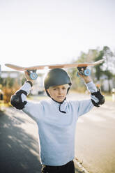 Portrait of boy carrying skateboard on head - MASF28220