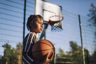 Kontemplatives Mädchen, das an einem sonnigen Tag mit einem Basketball wegschaut - MASF28224