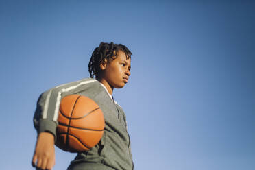 Mädchen schaut weg mit Basketball durch klaren Himmel - MASF28225